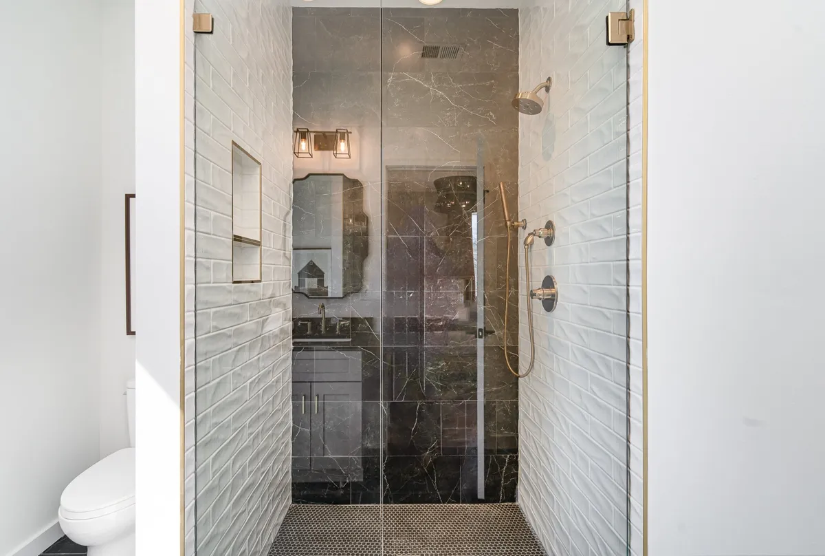 A luxurious, spa-inspired bathroom featuring a large glass shower enclosure, textured white wall tiles, a dark marble vanity, and elegant lighting. The design feels serene and inviting, perfect for self-care routines and relaxation.