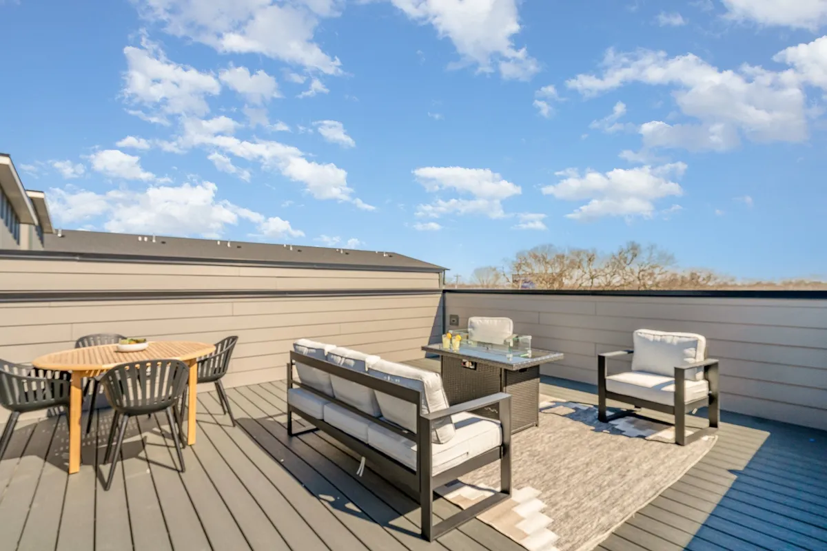 The image highlights an inviting outdoor seating area on a rooftop deck, featuring a small dining table set on a decorative rug. The setting basks in the warm glow of sunset, suggesting a perfect space for casual gatherings or intimate al fresco meals, with possibilities for stargazing against the Nashville skyline.