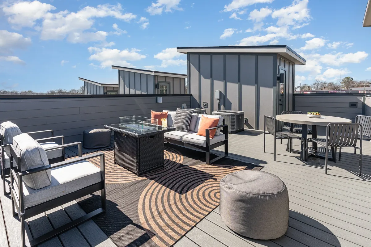 This exterior image captures an inviting outdoor seating area with a glass dining table and a decorative rug, set up for socializing and entertaining. The area is styled casually, perfect for groups to gather, enjoy meals, or unwind as the sun sets.
