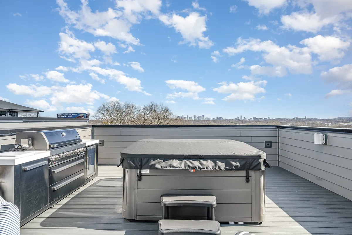 A stylish rooftop deck featuring an outdoor kitchen, a hot tub, and a stunning city skyline view. The space is set up for barbecuing and relaxing, with ample seating and ambient lighting that makes it perfect for both daytime and evening gatherings.