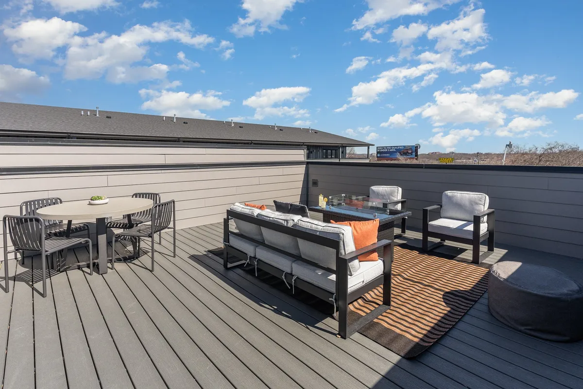 This exterior scene shows a relaxed rooftop or patio area furnished with a dining table, decorative rug, and seating, all beneath an open sky. The setting invites guests to enjoy meals, socialize, or relax in an alfresco environment.